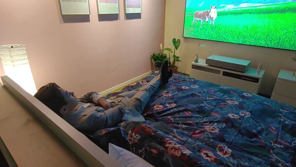 침실 룸에서 10cm 이내 간격 만으로 구현한 100인치 프로젝터 화면을 헨리가 침대에 누어 바라보고 있다.