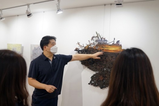 김민수 작가가 유디갤러리를 찾은 관객들에게 작품'낯익은 공허함2'를 설명하고 있다.